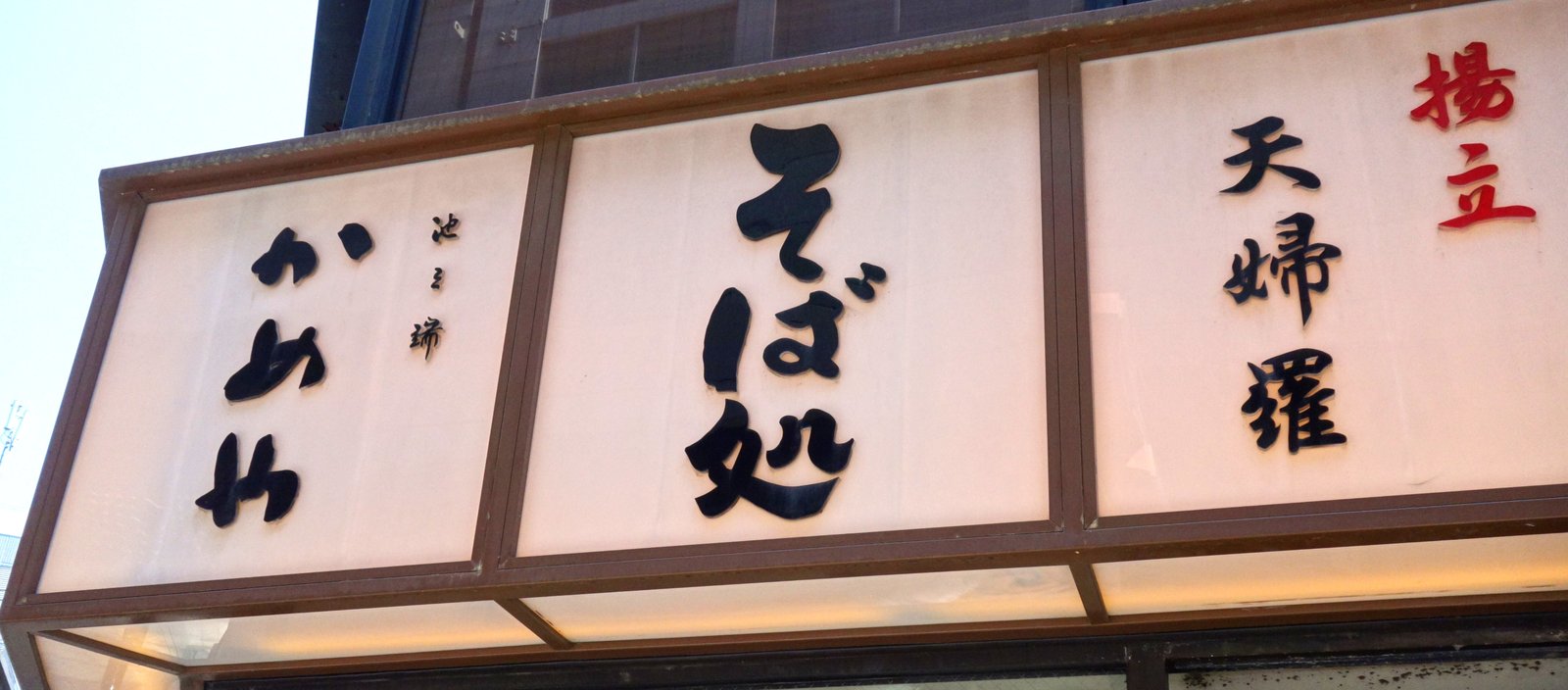 そば処 池之端 かめや 神田東口店の店外看板。「池之端 かめや」「そば処」「揚げたての天ぷら」と並ぶ