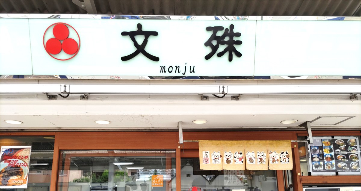 『文殊 monju』三つ巴ロゴの店名看板と招き猫の暖簾