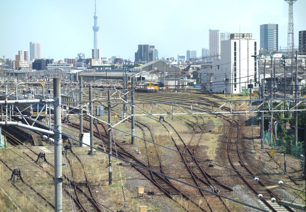 尾久車両センターの線路と車両。奥にTRAIN SUITE四季島の濃い色の編成、手前に黄色い保線用の車両