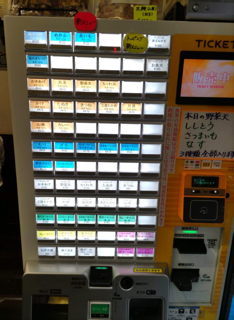 そばよし京橋店の券売機の全景。そば・うどんの各メニュー、トッピング、丼セット、土産の花かつおのボタンが並ぶ