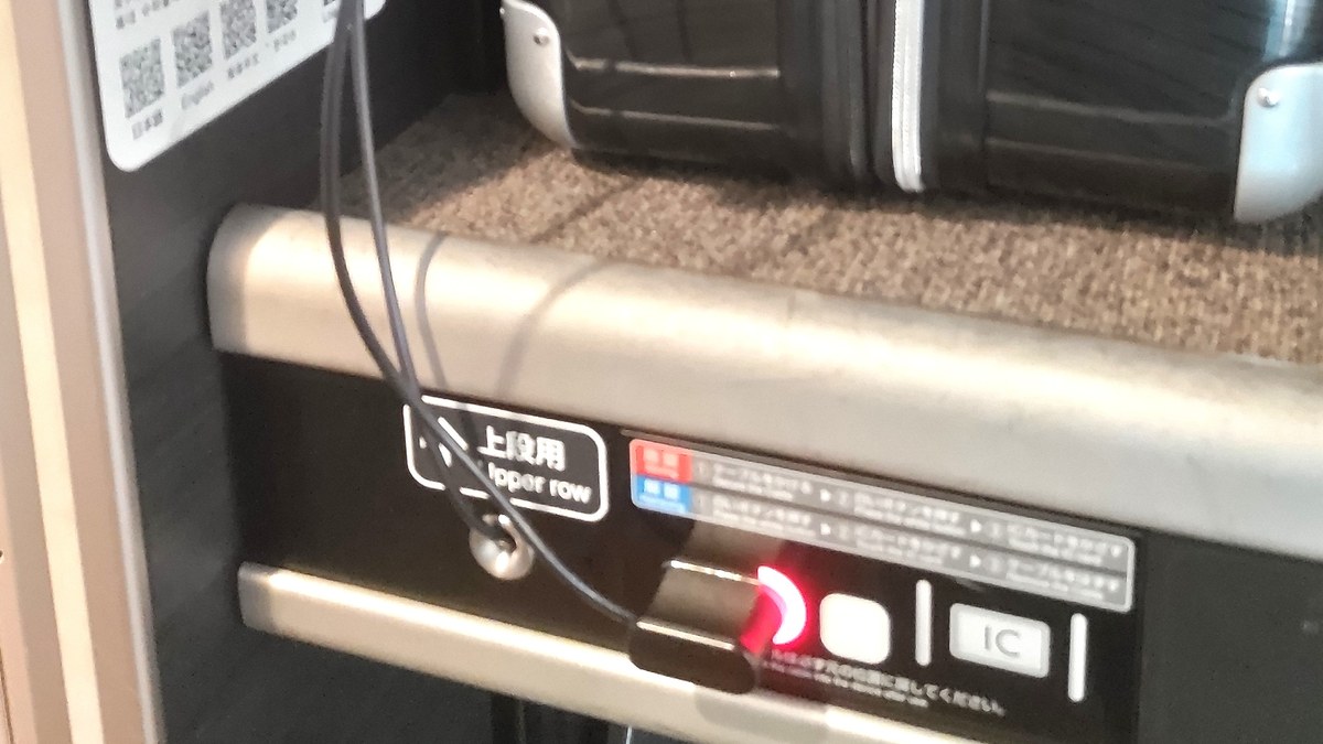 新幹線デッキの荷物置き場に置いたスーツケースと、赤いランプが点いた施錠パネル
