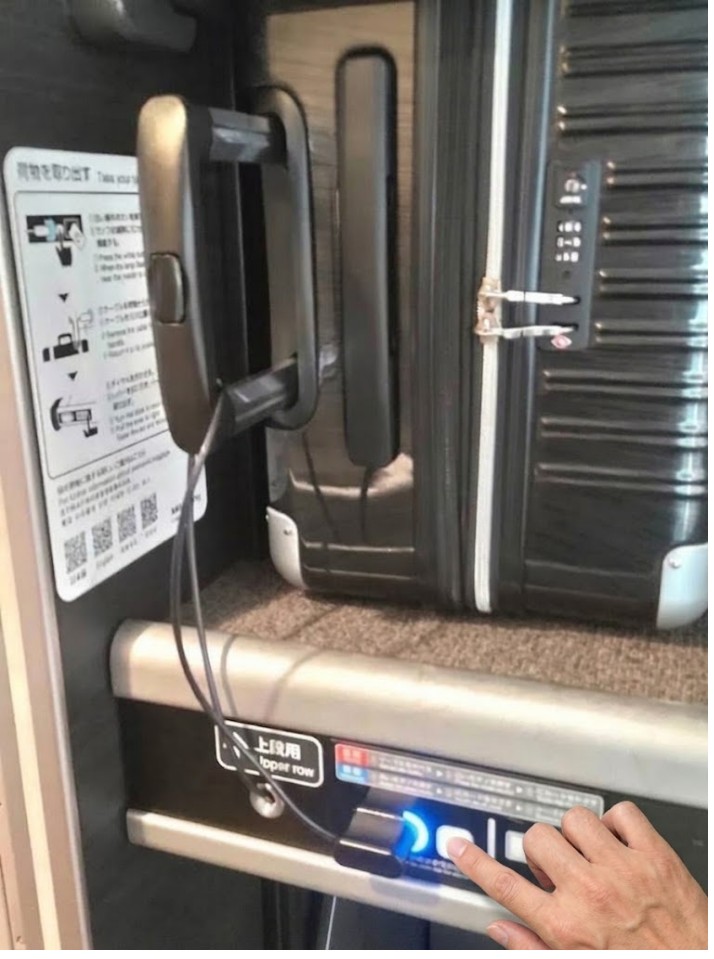 新幹線デッキ荷物置き場の操作パネル。青ランプ(解錠状態)の右にある白いボタンを人差し指で押している操作イメージ(現地写真に手を合成)